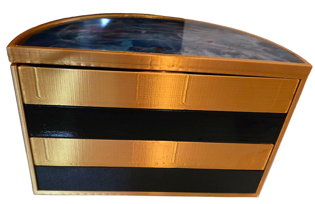 A 3D-printed decorative box with a gold-plated frame, black and gold striped body, and a blue marbled resin lid, shown on a light surface.